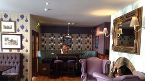 A room with a bar area, a tufted armchair, a patterned wall, and a mirror. - Ye Olde Griffin (March)