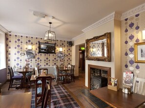 A dining area with a fireplace, a television, and patterned wallpaper. - Ye Olde Griffin (March)