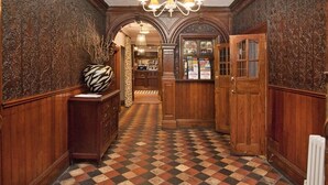 A hallway with patterned flooring, wooden walls, and a chandelier. - Ye Olde Griffin (March)