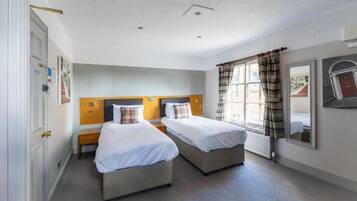 A hotel room with two beds, a wooden headboard, a window with curtains, and a radiator.