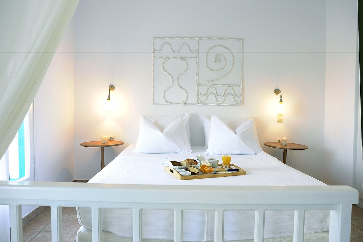 A neatly made bed with white linens, two bedside tables with lamps, a tray of breakfast items, and a decorative wall piece.