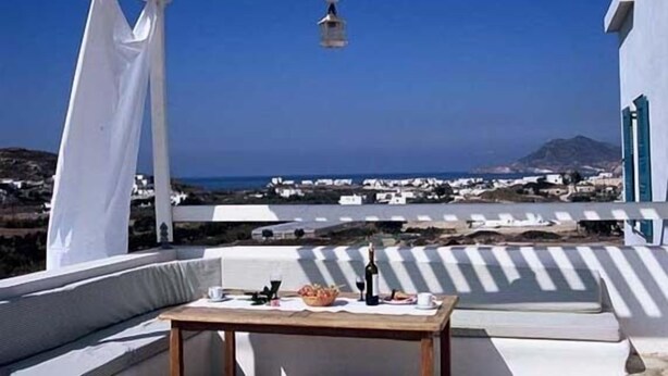 A terrace with a table set for dining, overlooking a coastal village and the sea. - Kostantakis Winery & Residence (Milos)