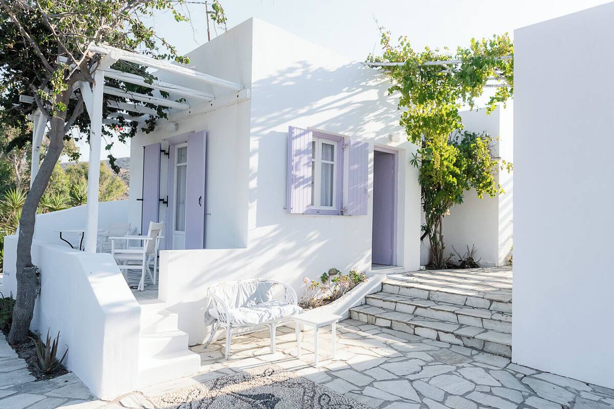 A white building with a covered patio, stone steps, and a white chair.