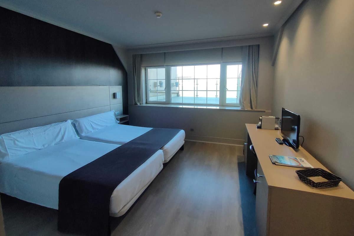 A hotel room with a large bed, a desk with a computer, and a window with a view of the sea.