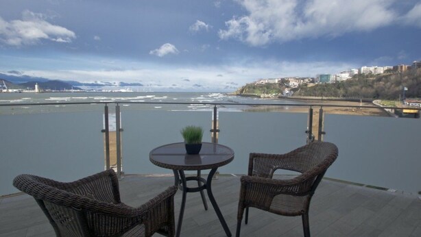 A terrace with wicker chairs and a table, overlooking a river with a bridge and buildings in the background. - Hotel Igeretxe (Getxo)