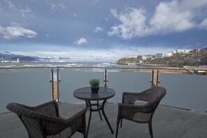 A terrace with wicker chairs and a table, overlooking a river with a bridge and buildings in the background. - Hotel Igeretxe (Getxo)