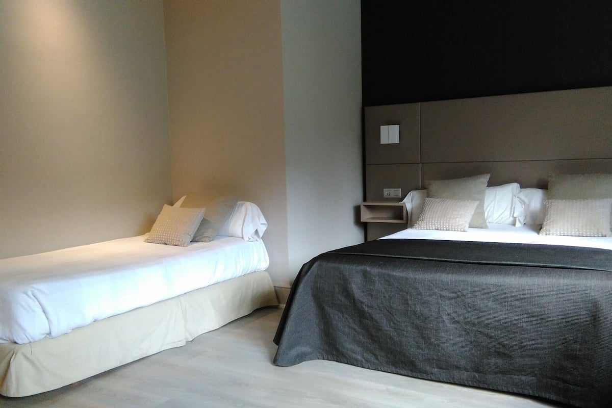 A hotel room with two single beds, a large bed, and a nightstand with a lamp.