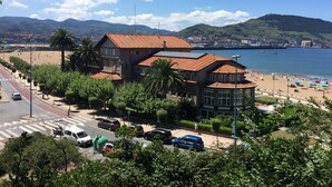 A coastal building with a red-tiled roof, adjacent to a beach with umbrellas and people. - Hotel Igeretxe (Getxo)
