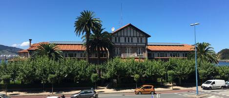 A building with a red-tiled roof and a balcony, surrounded by greenery and a clear blue sky.