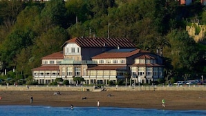 A large, multi-story building with a prominent balcony area, situated near a beach with people in the water. - Hotel Igeretxe (Getxo)