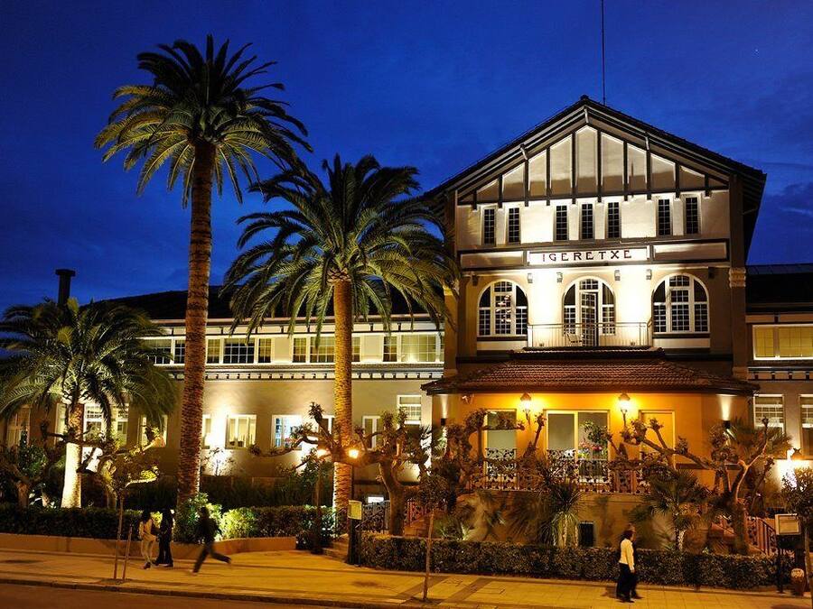Un hotel de estilo arquitectónico clásico, con una entrada destacada que presenta ventanas arqueadas y un balcón.