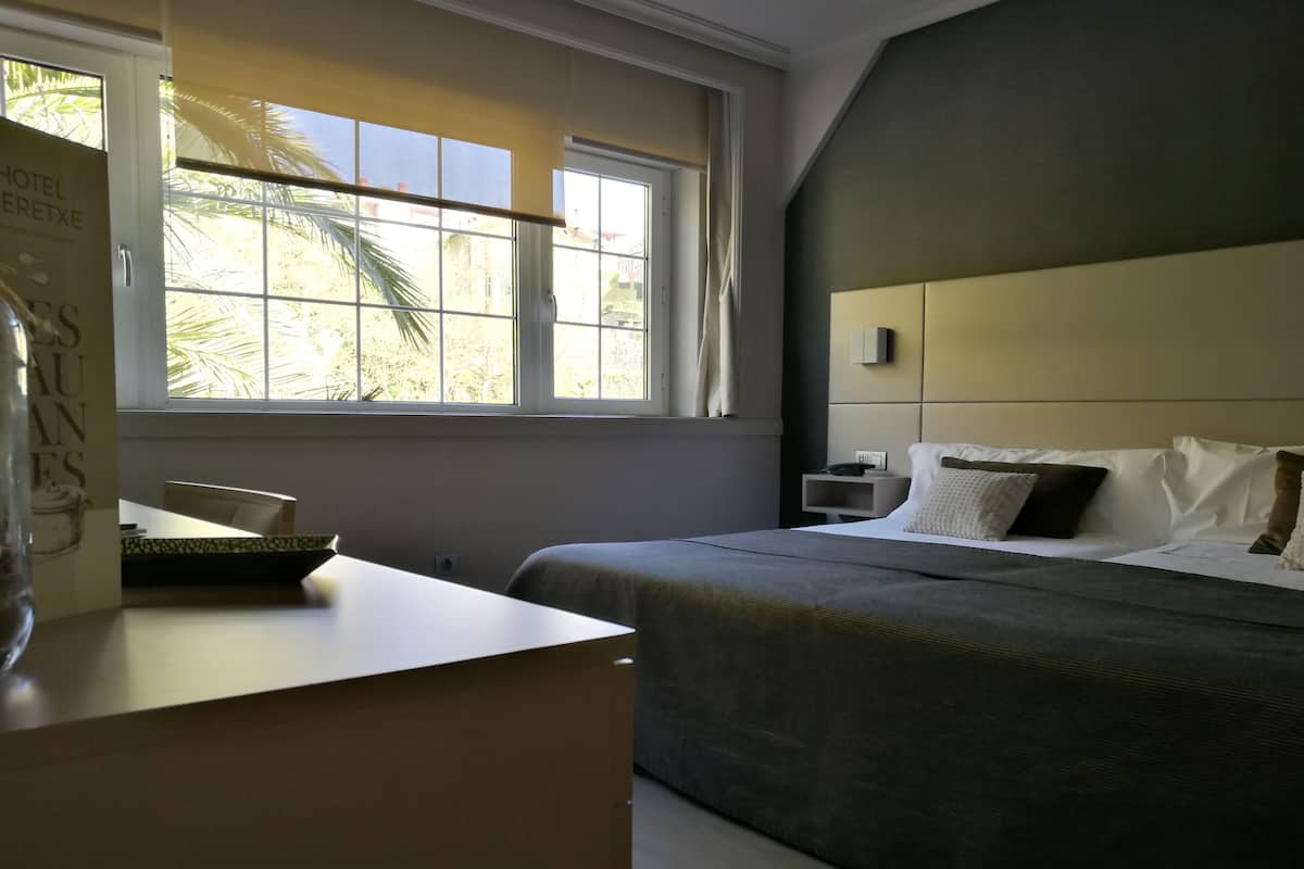 A hotel room with a bed, bedside table, and a window with a view of palm trees.