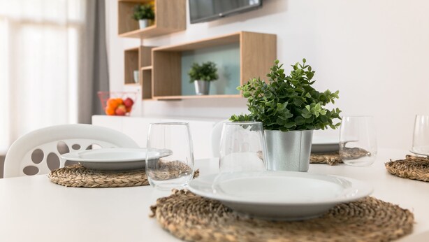 A dining table set with plates, glasses, and a potted plant. - RVApartaments Benelux (Castell-Platja d'Aro)