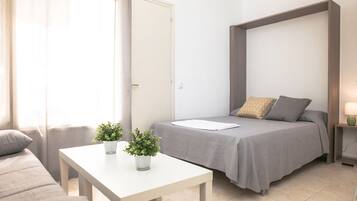 Un dormitorio moderno con una cama, una mesita con plantas, un sofá y una mesita de noche con una lámpara.