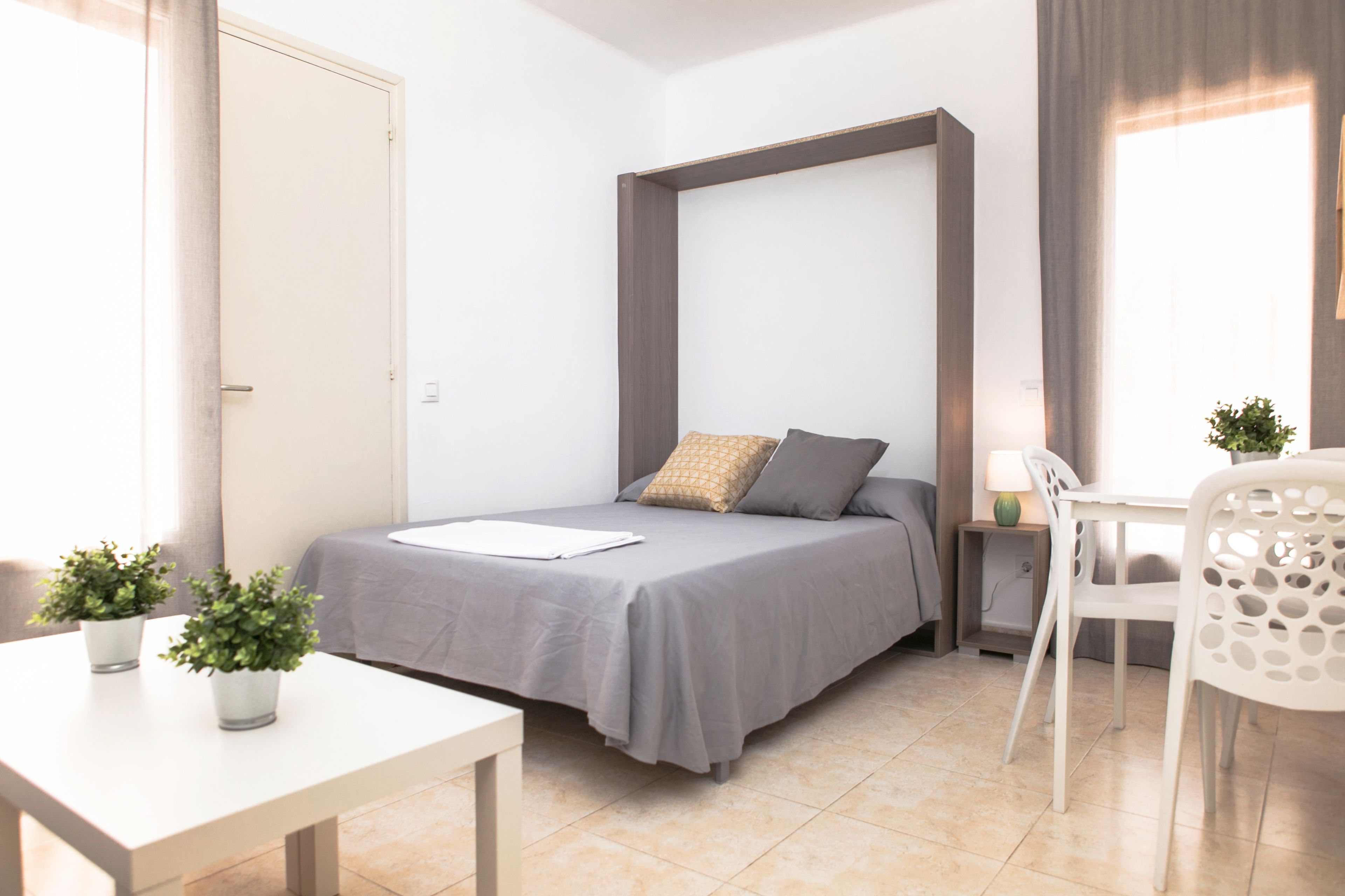 A compact bedroom with a bed, bedside table, and a small desk area.