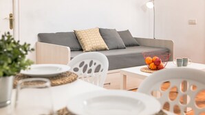A modern living room with a grey sofa, white chairs, and a dining table with plates and a fruit bowl. - RVApartaments Benelux (Castell-Platja d'Aro)
