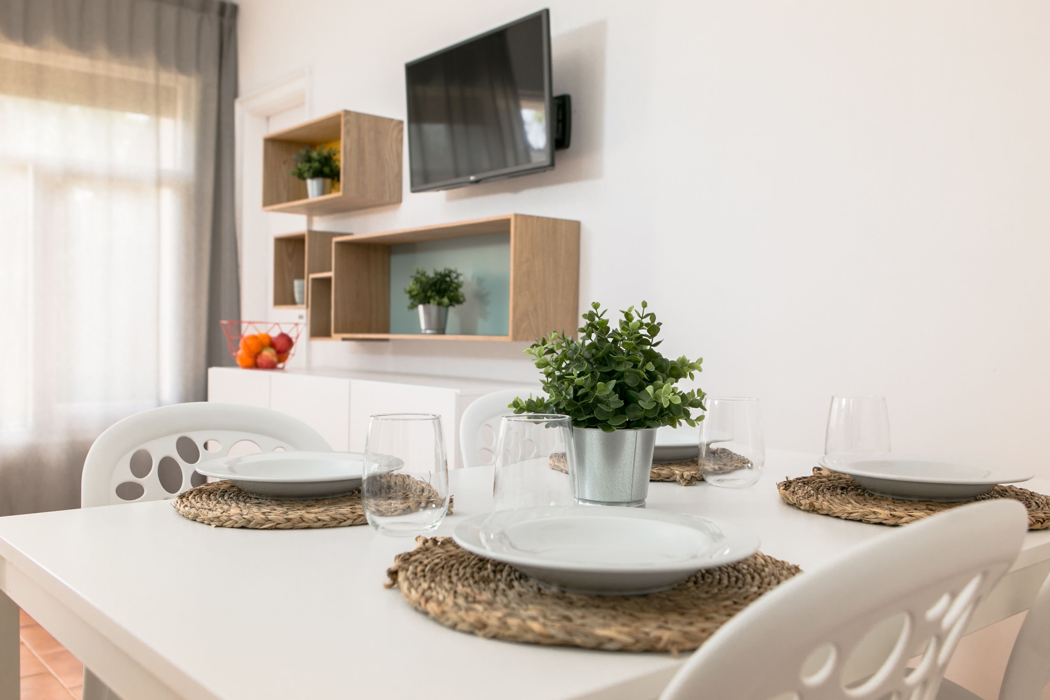 Una mesa de comedor dispuesta con platos, vasos y una planta en maceta.