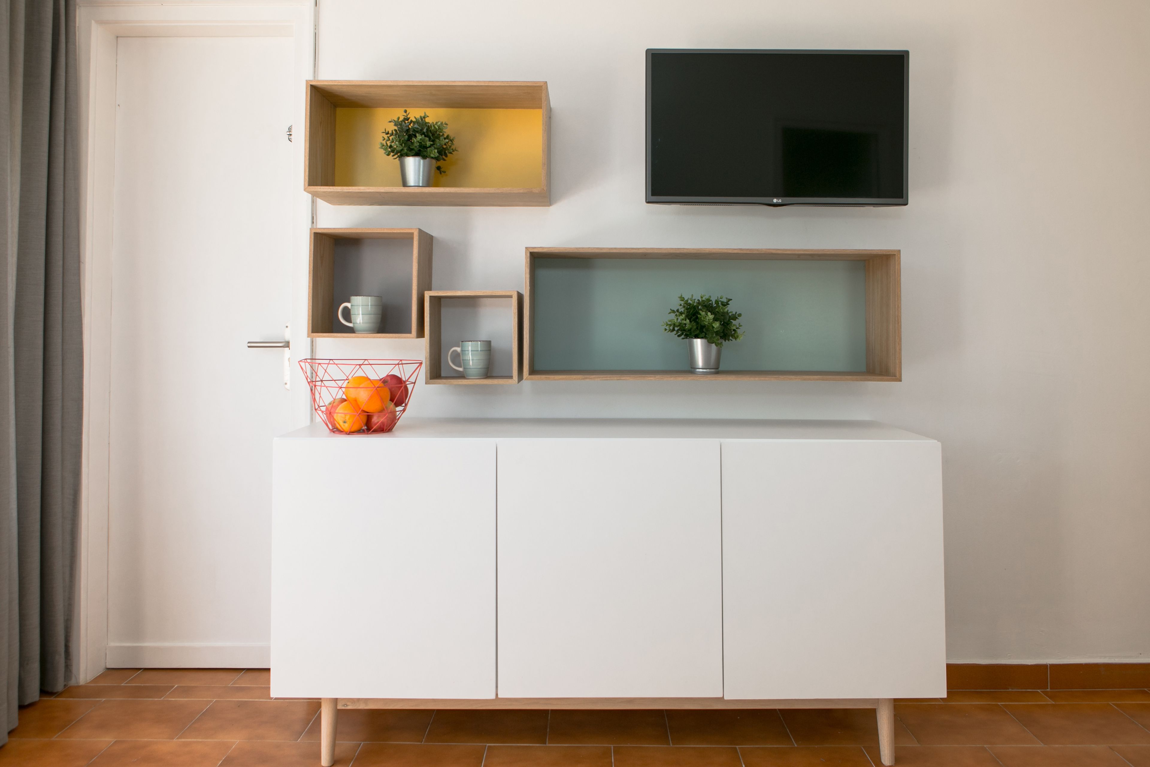 Un mueble blanco con estantes, un televisor y una cesta de naranjas.