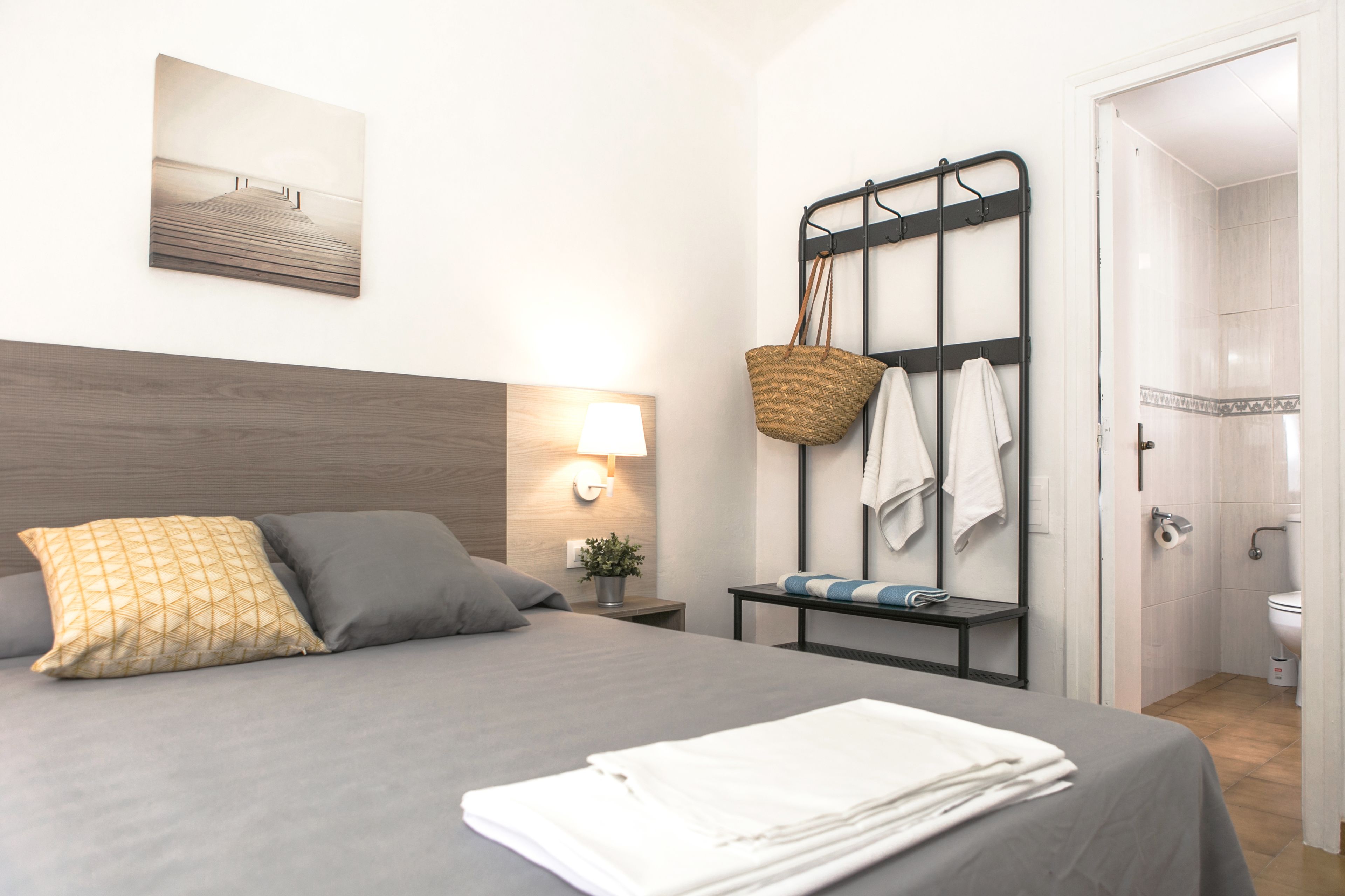 A neatly made bed with pillows, a bedside lamp, a wall-mounted towel rack, and a small table with a plant.