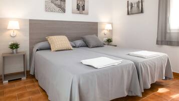 A double bed with grey linens, two bedside tables with lamps, and a wall with three framed pictures.