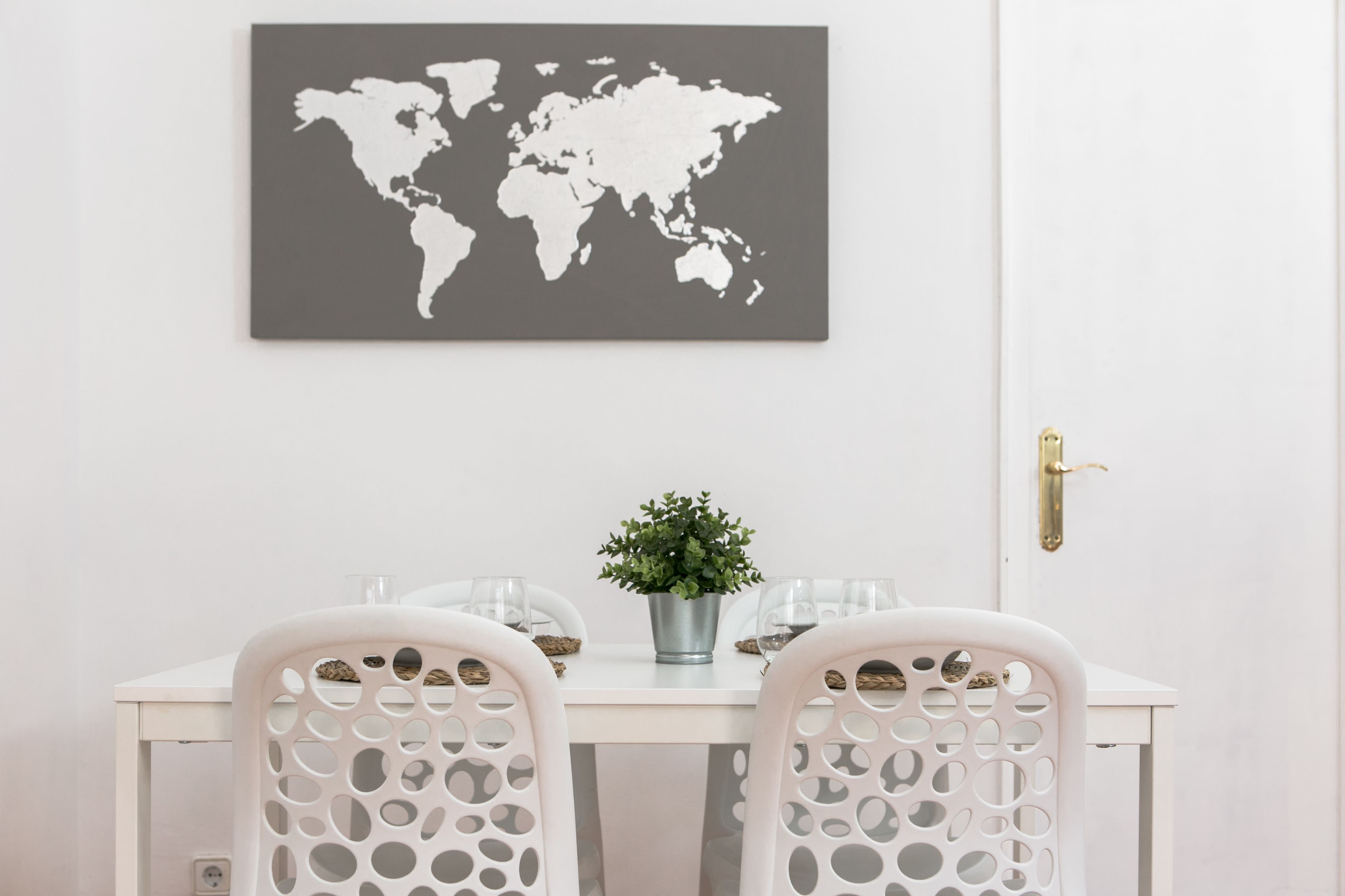 Un coin repas avec une table blanche, deux chaises, une plante en pot et une carte du monde accrochée au mur.