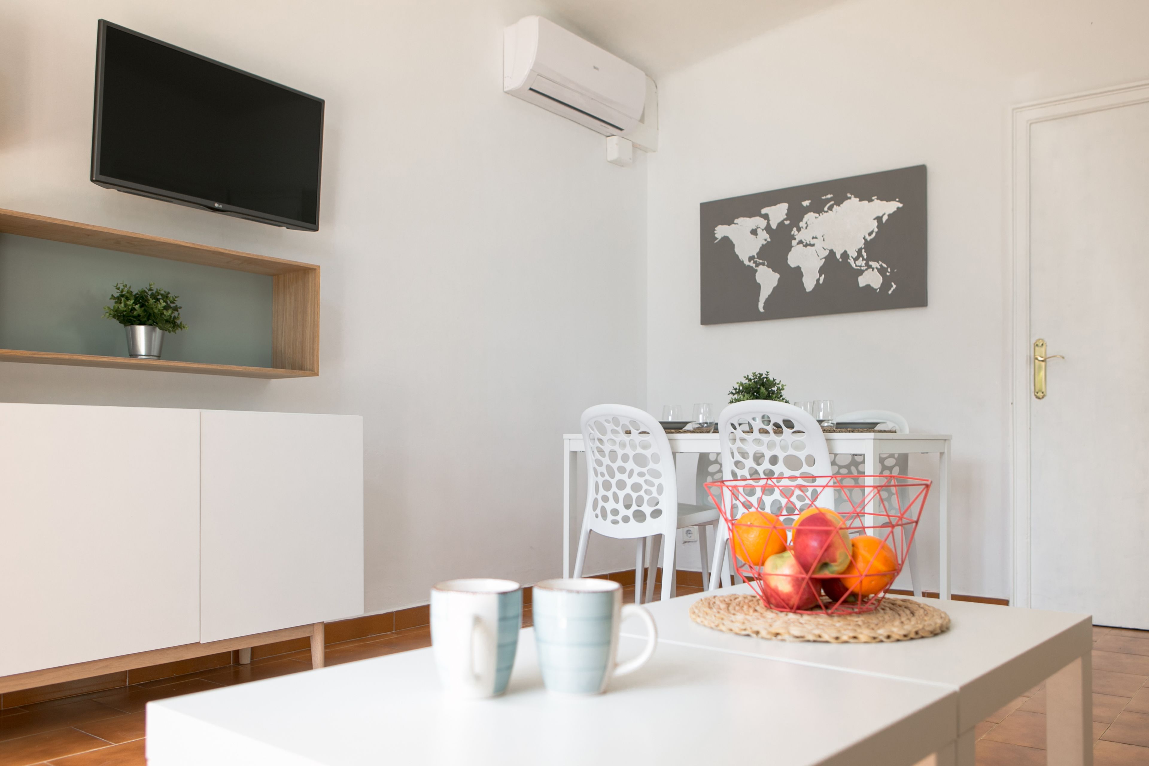 A modern dining area with a white table, chairs, and a fruit basket.