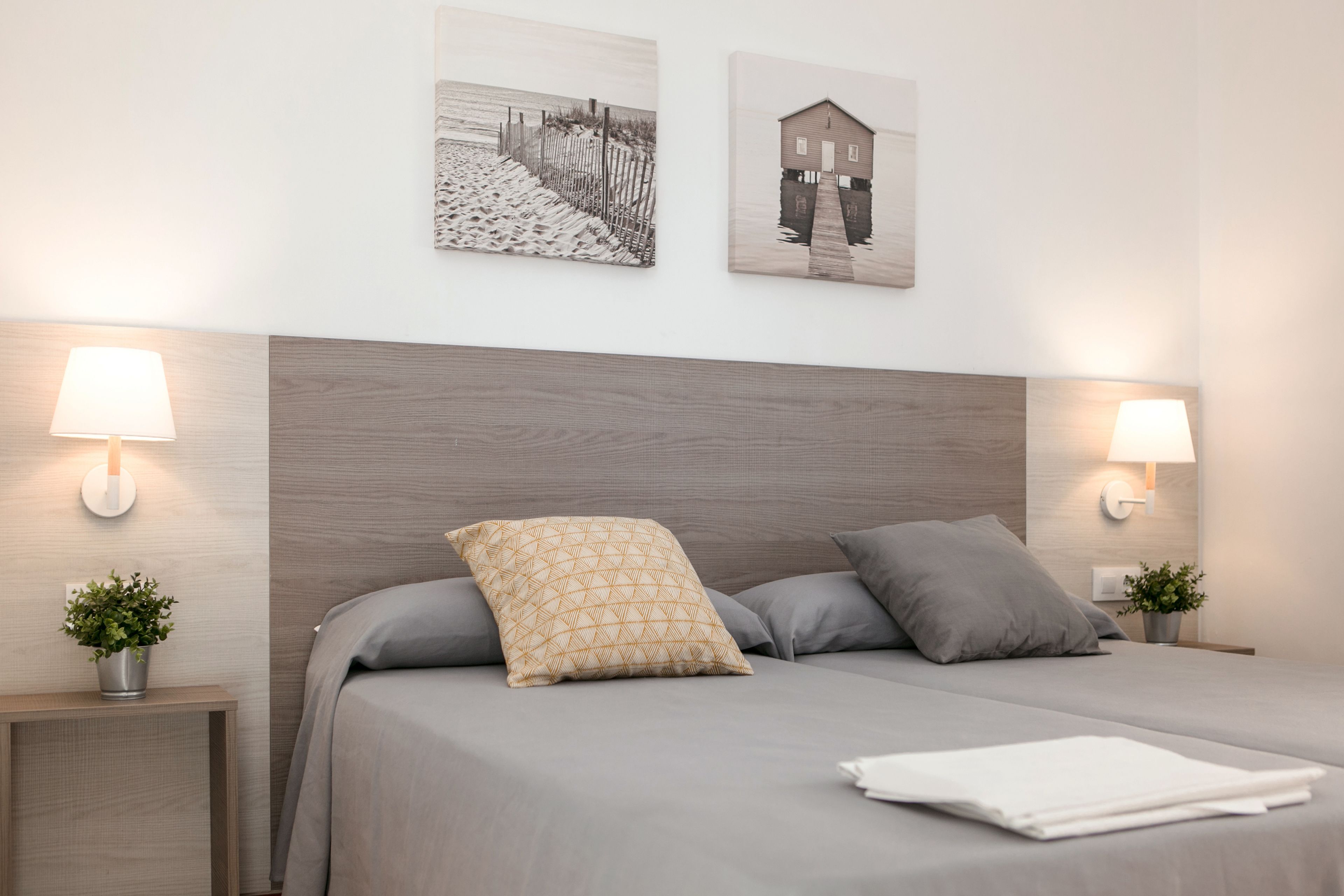 A neatly made bed with a headboard, two bedside lamps, and two wall-mounted pictures.