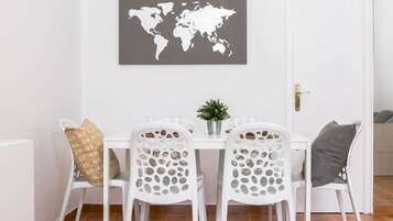 Un comedor con una mesa y sillas blancas, un mapa del mundo en la pared y una planta en maceta sobre la mesa.