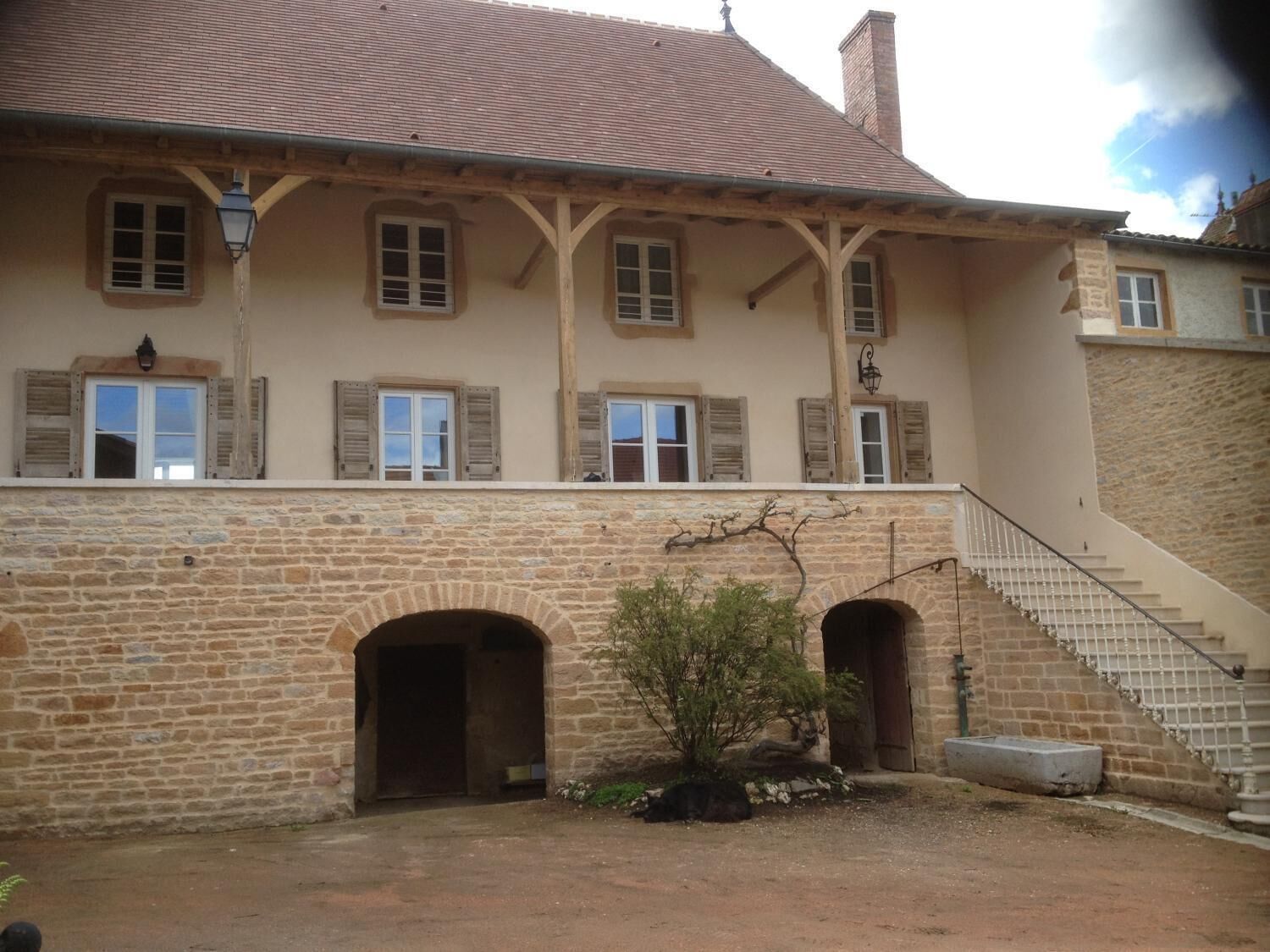 Un bâtiment en pierre de deux étages, doté d’un toit en tuiles, de nombreuses fenêtres avec volets et d’un escalier central menant à un étage supérieur.