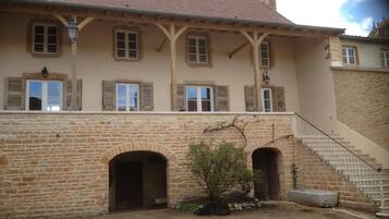 Un bâtiment en pierre de deux étages, doté d’un toit en tuiles, de nombreuses fenêtres avec volets et d’un escalier central menant à un étage supérieur.