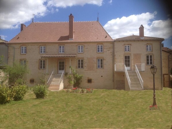A two-story stone building with a red-tiled roof, a central entrance with a staircase, and a small garden area with a lamp post. - Le Logis d'Azé (Aze)