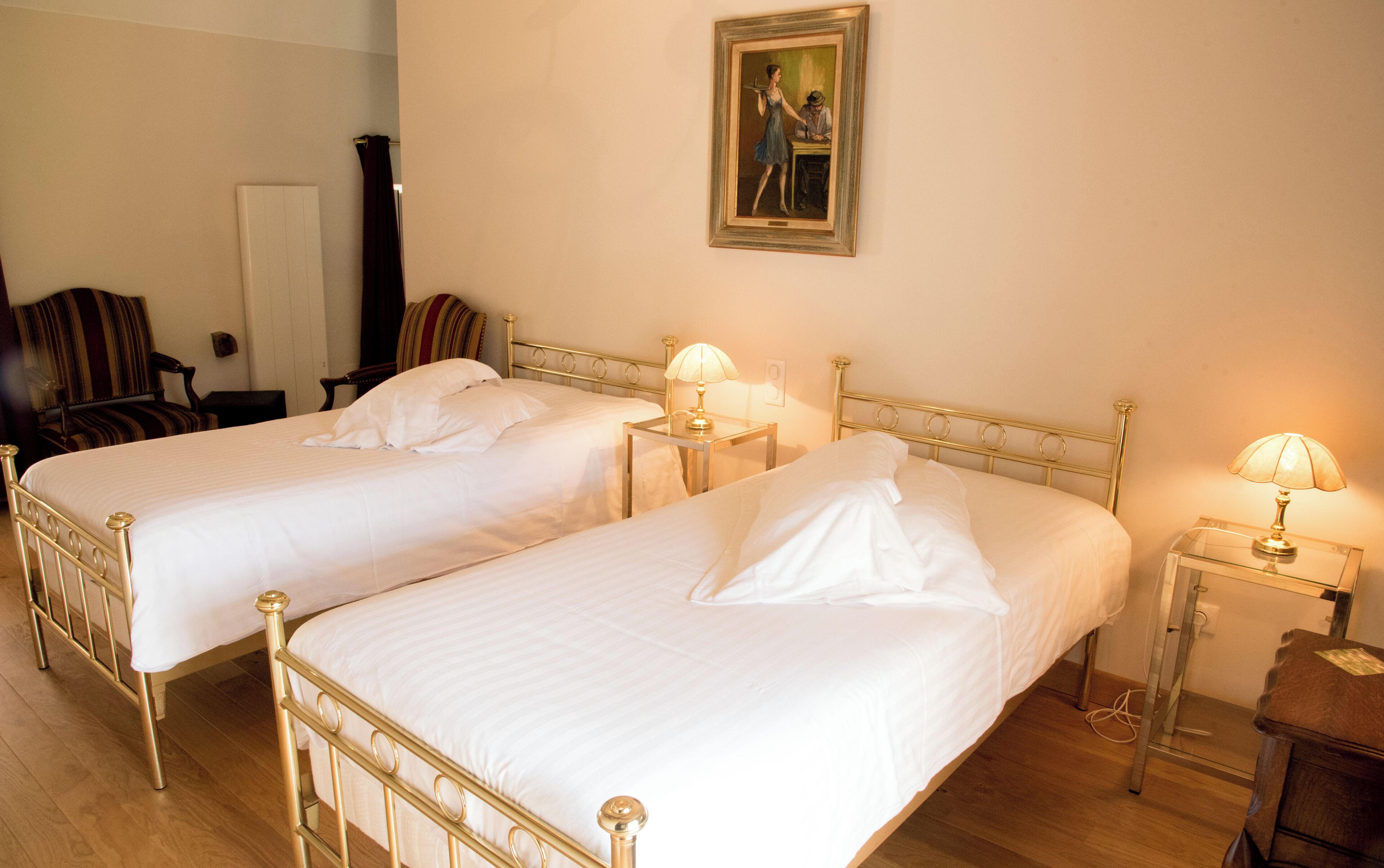 Two single beds with gold frames, white linens, and bedside lamps.