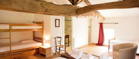 A room with bunk beds, a chair, a table with towels, and wooden beams on the ceiling.