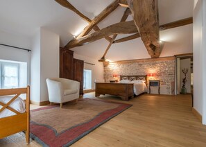 A bedroom with a wooden ceiling, a stone wall, a bed, a chair, and a nightstand with lamps. - Le Logis d'Azé (Aze)