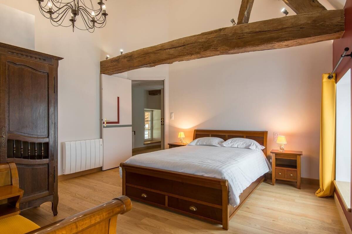 Quarto com cama de madeira, mesas de cabeceira, um candelabro e uma viga de madeira no teto.