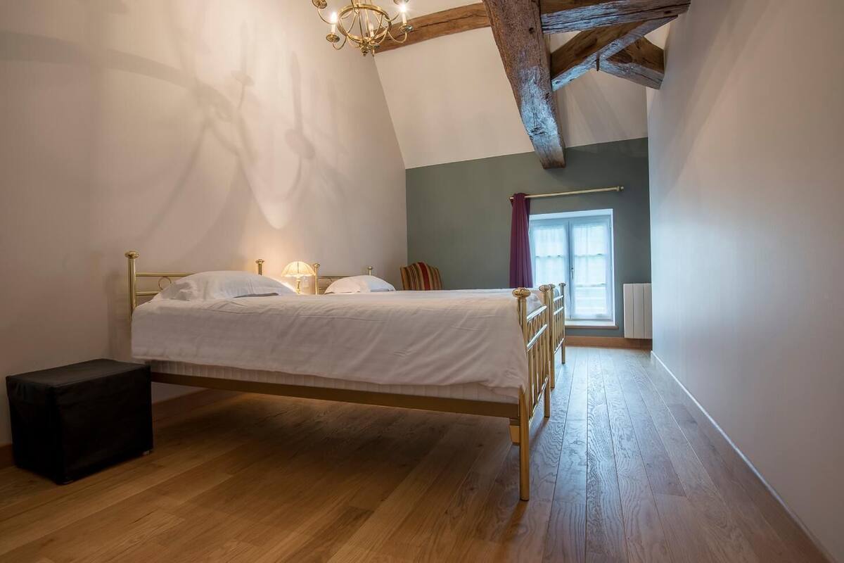 Quarto com cama, mesa de cabeceira, luminária, janela com cortinas e radiador.