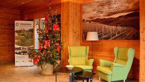 Un intérieur en bois, avec un sapin de Noël, deux fauteuils verts, une petite table et une affiche accrochée au mur.