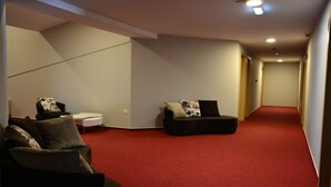 Un couloir avec un tapis rouge, deux canapés noirs ornés de coussins à motifs et une petite table d’appoint blanche.