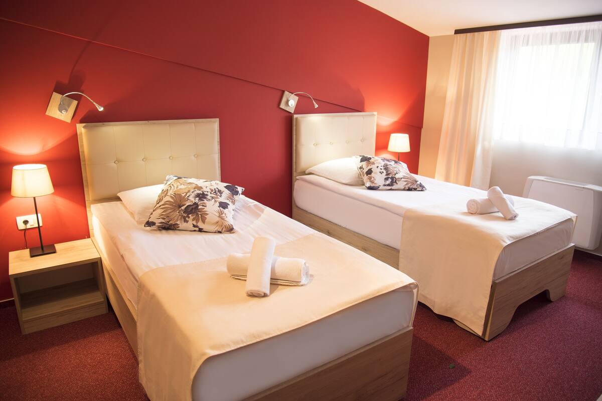 Habitación de hotel con dos camas, cada una con cabecero, lámparas de noche y una ventana con cortinas.