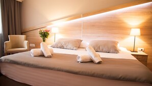 Une chambre d’hôtel avec un grand lit, deux tables de chevet, une chaise et une petite table de nuit avec une lampe.