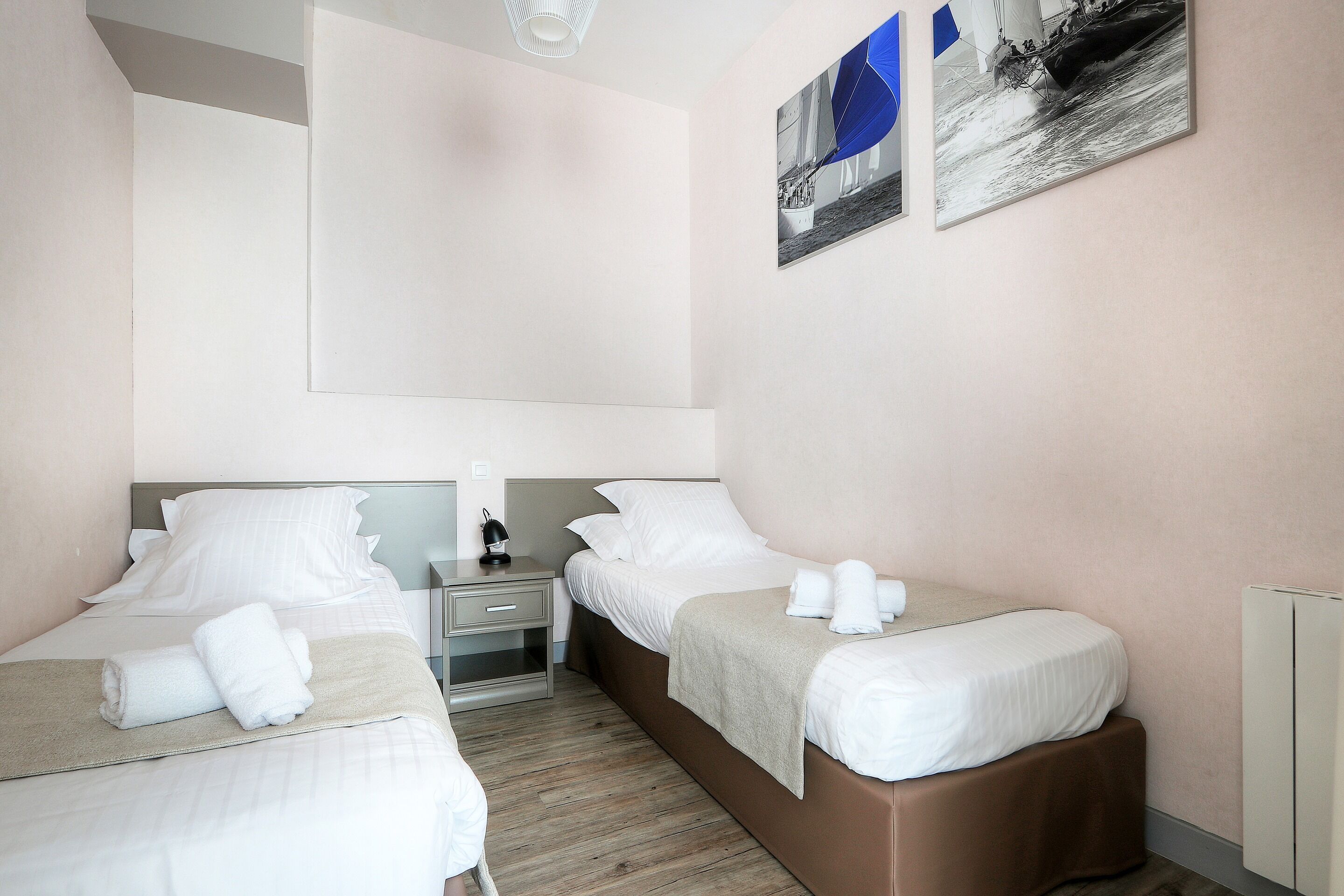 A hotel room with two beds, a nightstand, a lamp, and two framed pictures on the wall.