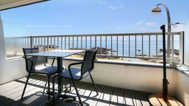 Een balkon met een tafel en stoelen, met uitzicht op een strand met een hek en een lantaarnpaal.