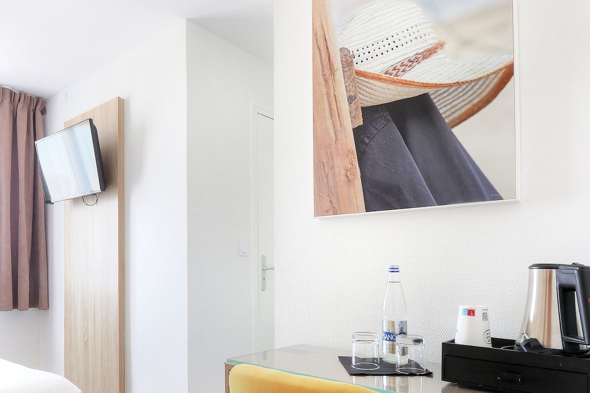 Ein Hotelzimmer mit Bett, Schreibtisch mit Stuhl, Fernseher, einem Gemälde und einer Kaffeemaschine.