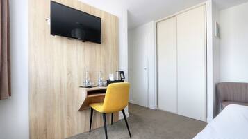 A hotel room with a wooden accent wall, a flat-screen TV mounted above a desk, a yellow chair, a bed, and a wardrobe.