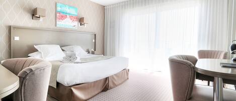 A hotel room with a bed, two chairs, a small table, and a painting on the wall.
