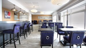 Een moderne eethoek met hoge tafels en blauwe stoelen met bekleding en metalen ringen.