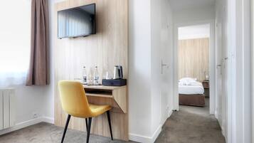 Habitación de hotel con escritorio de madera, televisor montado en la pared, cama con ropa blanca y baño visible a través de una puerta abierta.