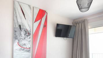 Una camera d'hotel con un letto, una cassettiera bianca, una poltrona blu, un quadro astratto di grandi dimensioni, una televisione a schermo piatto montata a parete e una finestra con tende.