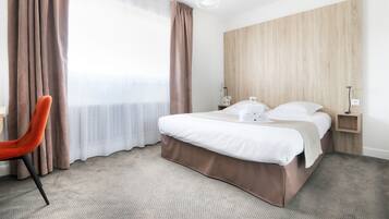 Habitació d'hotel amb llit, una cadira, una taula de nit i una finestra gran amb cortines.