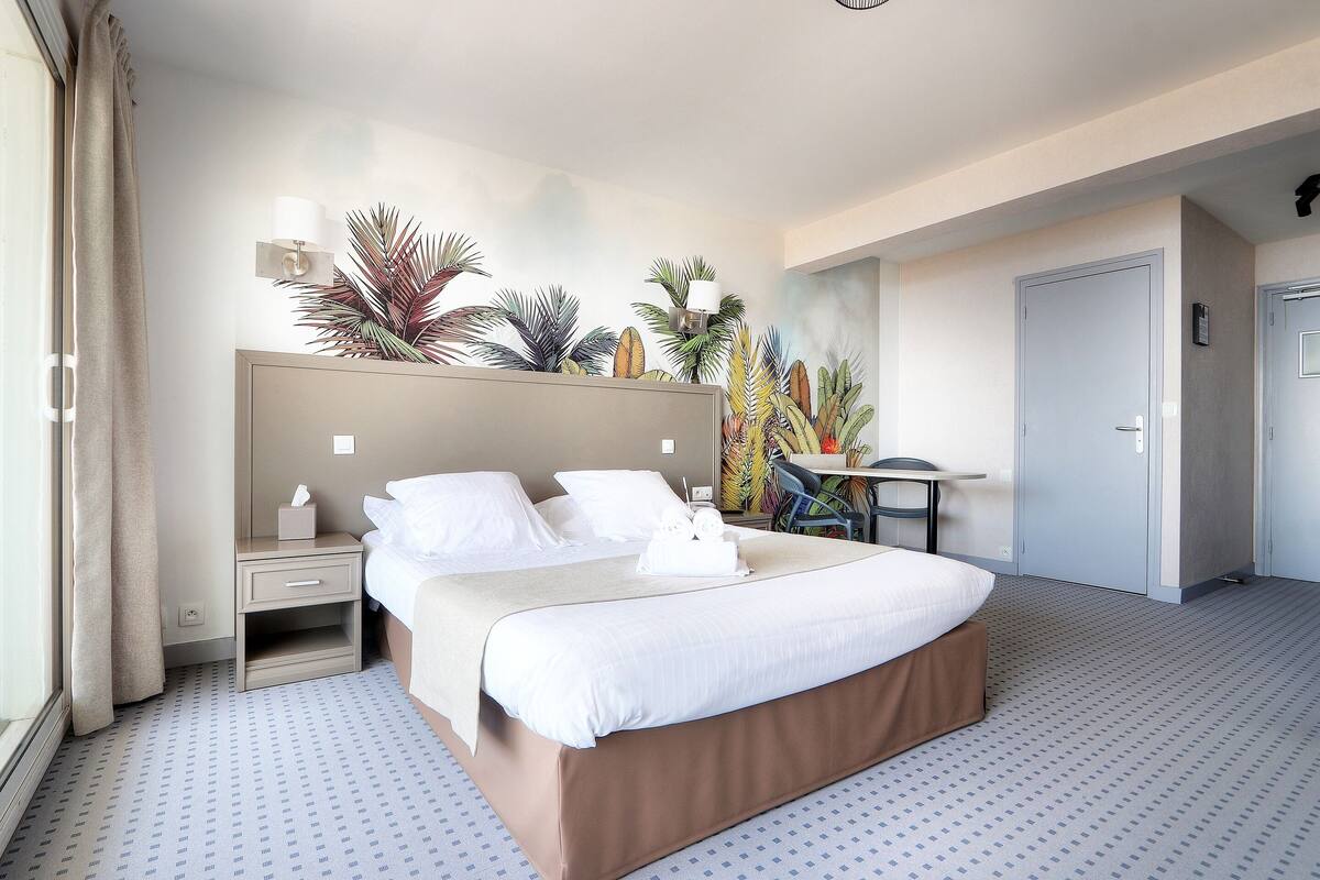 Ein Hotelzimmer mit einem großen Bett, Nachttischen, einem Schreibtisch und einem Sessel.